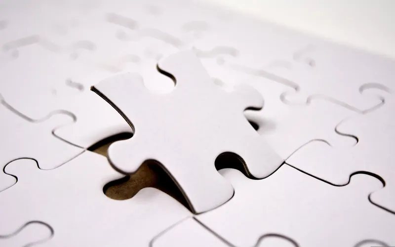 Symbolbild: Weißes Puzzleteil wird in die passende Lücke eines weißen Puzzles gesetzt